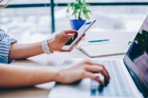 Woman with phone in one hand and laptop in the other 1024x576